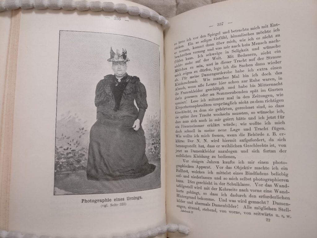 Double-page spread of a book from the display. On the left is a photograph of a person wearing a 19th-century women’s gown and hat, captioned “Photographie eines Urnings”. The German text on the right is a page from the person’s own account of their love of women’s clothes.